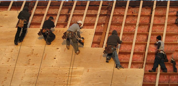 five workers on roof working on putting plywood down before roofing materials